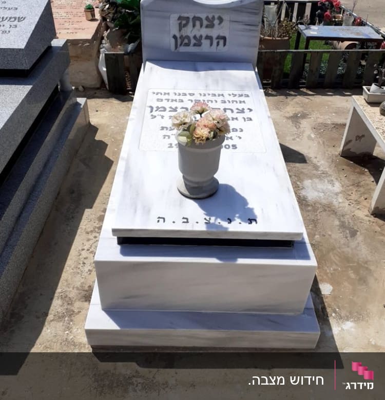 מצבה לבנה עם כיתוב בעברית ואגרטל פרחים